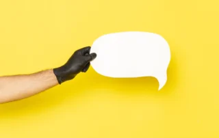 Braccio con guanto nero che tiene un fumetto bianco su sfondo giallo, a rappresentare la chat di assistenza clienti per siti web.